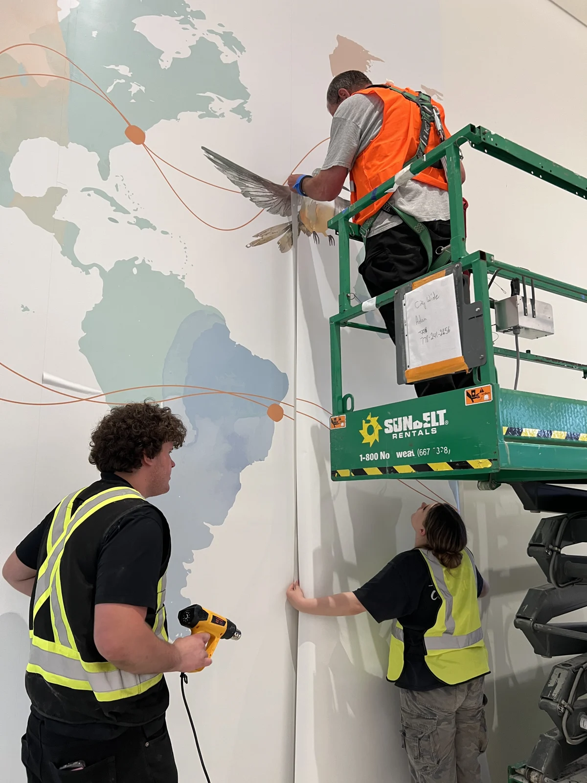 Vivid installation crew applying the world map graphic using a lift